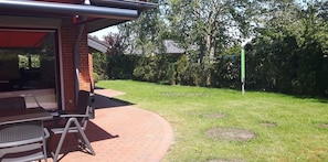 A covered outdoor seating area with a brick wall, a metal table, and a chair. - Vacation home for 6 guests, 72 m², in Sankt Peter-Ording (318292) (Sankt Peter-Ording)