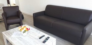 A living room with a dark brown sofa, a wooden coffee table with a vase of flowers, and two remote controls. - Vacation home for 6 guests, 72 m², in Sankt Peter-Ording (318292) (Sankt Peter-Ording)