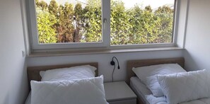 Makuuhuoneessa on kaksi sänkyä, ikkunasta avautuu näkymä puita kohden, ja seinälle on asennettu latausasema.