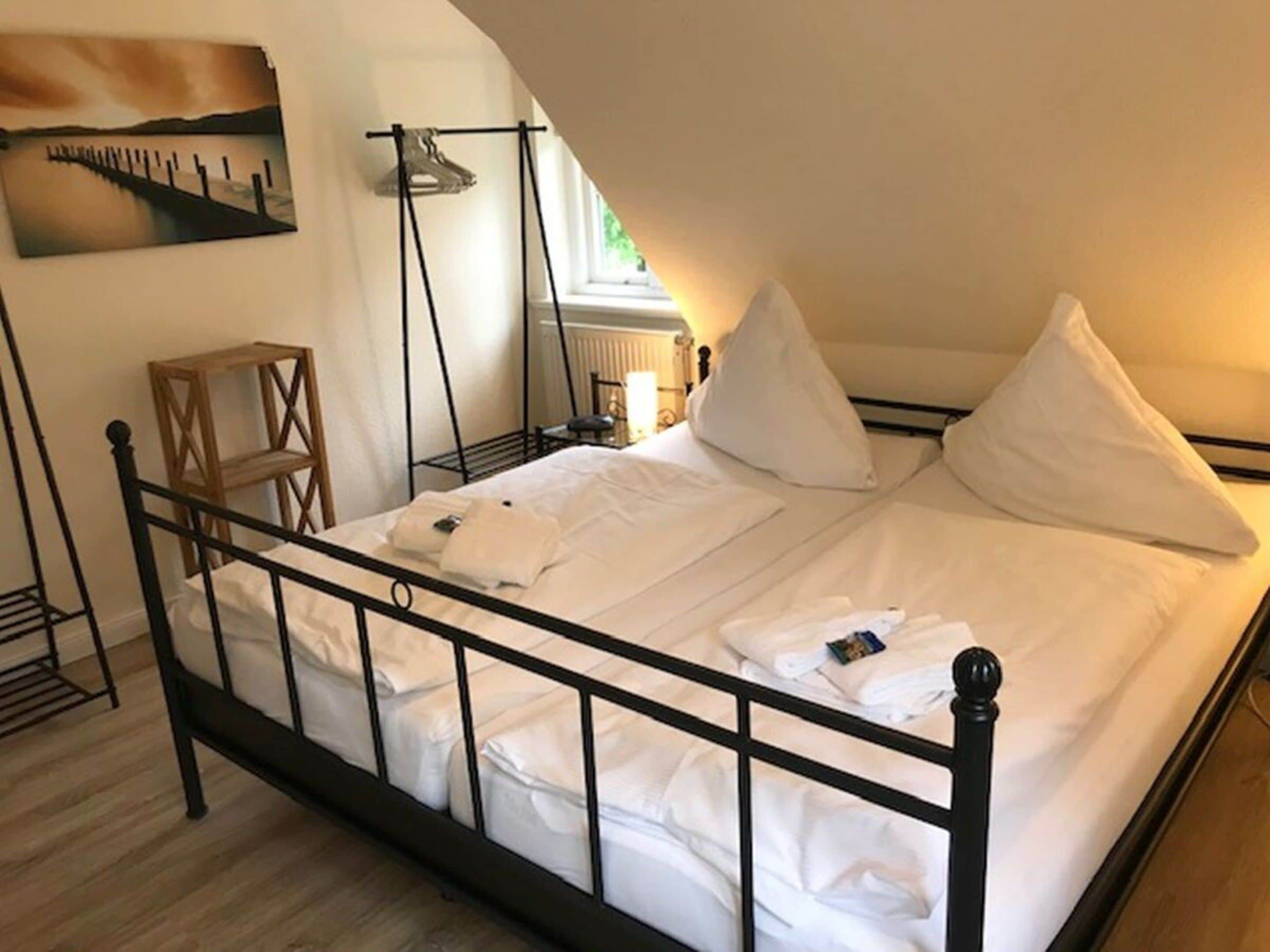 Ein ordentlich bezogenes Bett mit weißen Leinen, einem hölzernen Kopfteil und einem Bild an der Wand.