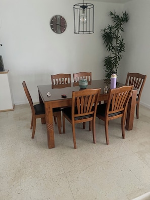A dining area with a wooden table and chairs, a potted plant, a clock, and a hanging light fixture. - Perfect 3-bedroom townhome with AC in charming Exchange Ocho Rios (Ocho Rios)