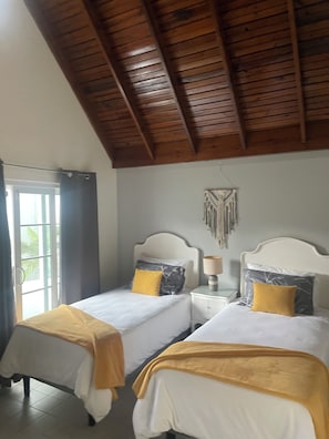 A room with two beds, a wooden ceiling, a wall decoration, and a window with curtains. - Perfect 3-bedroom townhome with AC in charming Exchange Ocho Rios (Ocho Rios)