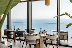 A modern dining area with a view of the sea, featuring a round table, chairs, and a hanging light fixture. - Mercury Suites Elegant Apartment (St. Julian's)