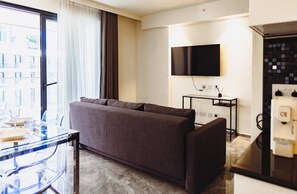 A modern hotel room with a sofa, a glass table, a flat-screen TV mounted on the wall, and a minibar. - Mercury Suites Prestige Stay, Pool Access (St. Julian's)