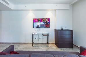 A modern living room with a flat-screen TV mounted on the wall, a glass-top coffee table, a dark wooden cabinet, and a grey sofa. - Mercury Suites Refined Living, Pool Access (St. Julian's)