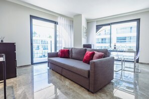 A modern living room with a grey sofa, a glass coffee table, and a view of a cityscape through large windows. - Mercury Suites Refined Living, Pool Access (St. Julian's)
