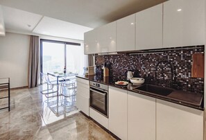 A modern kitchen with a large island, a dining area with a glass table, and a view through the window. - Mercury Suites 2BR Luxury Hideaway, Pool Access (St. Julian's)