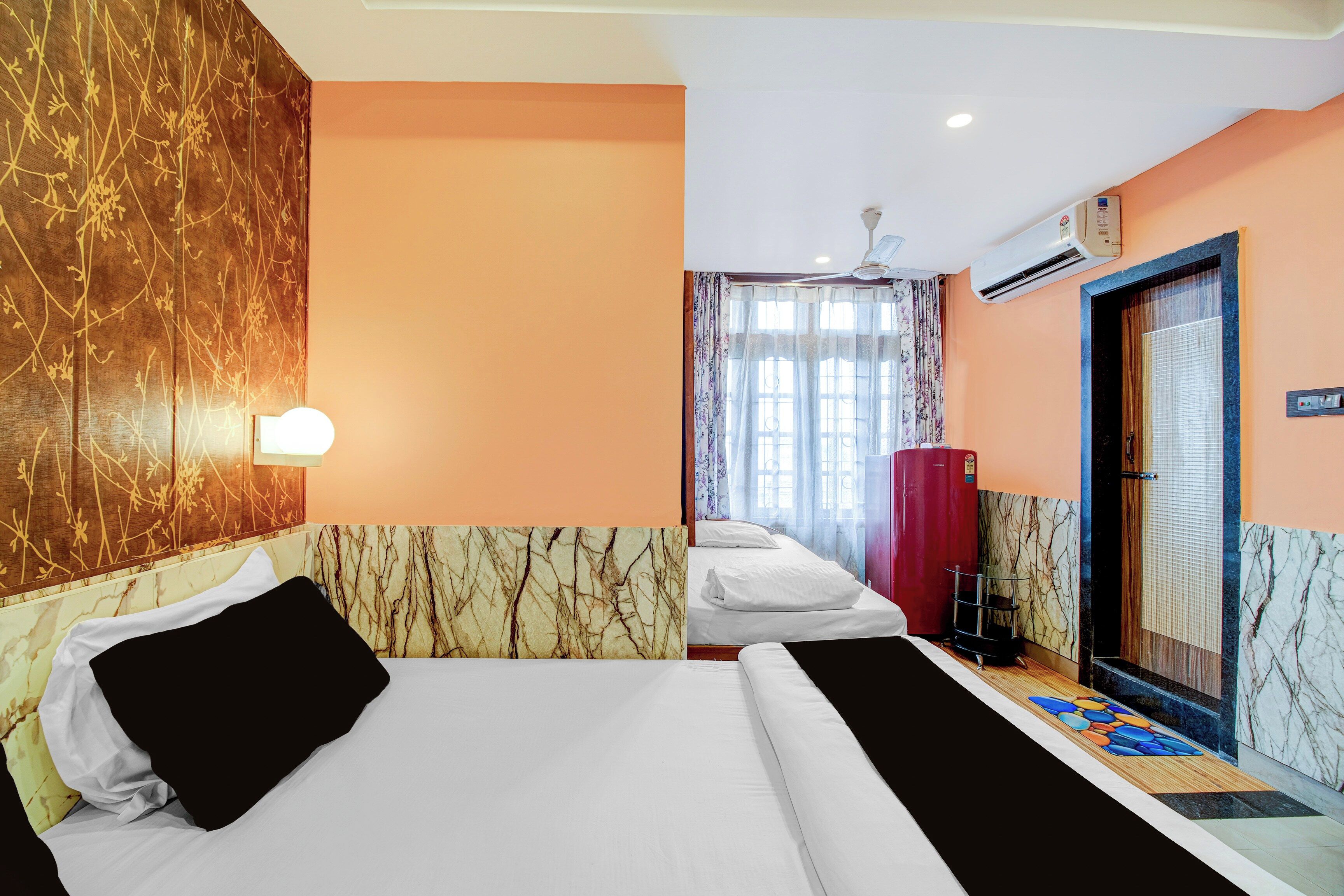 A hotel room with two beds, a marble-patterned wall, a window with curtains, an air conditioning unit, and a door with a handle.