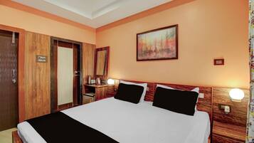 A hotel room with a large bed, wooden headboard, a painting on the wall, and a small desk with a lamp.