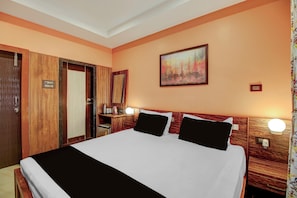 A hotel room with a large bed, wooden headboard, a painting on the wall, and a small desk with a lamp. - Super Collection O Downtown Hospital (Guwahati)
