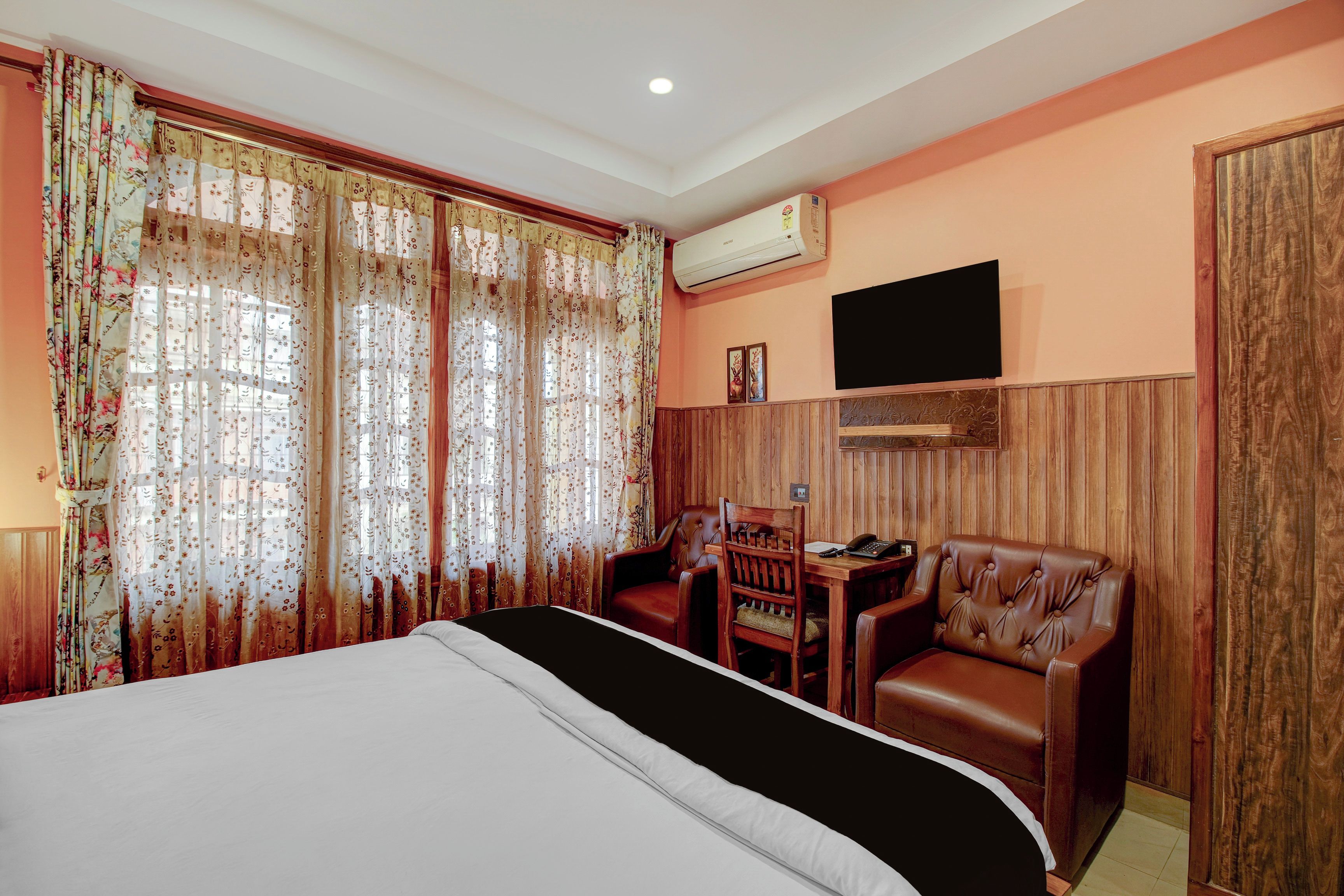 Een hotelkamer met een bed, twee leren fauteuils, een tafeltje, een airconditioning en een aan de muur bevestigde televisie.
