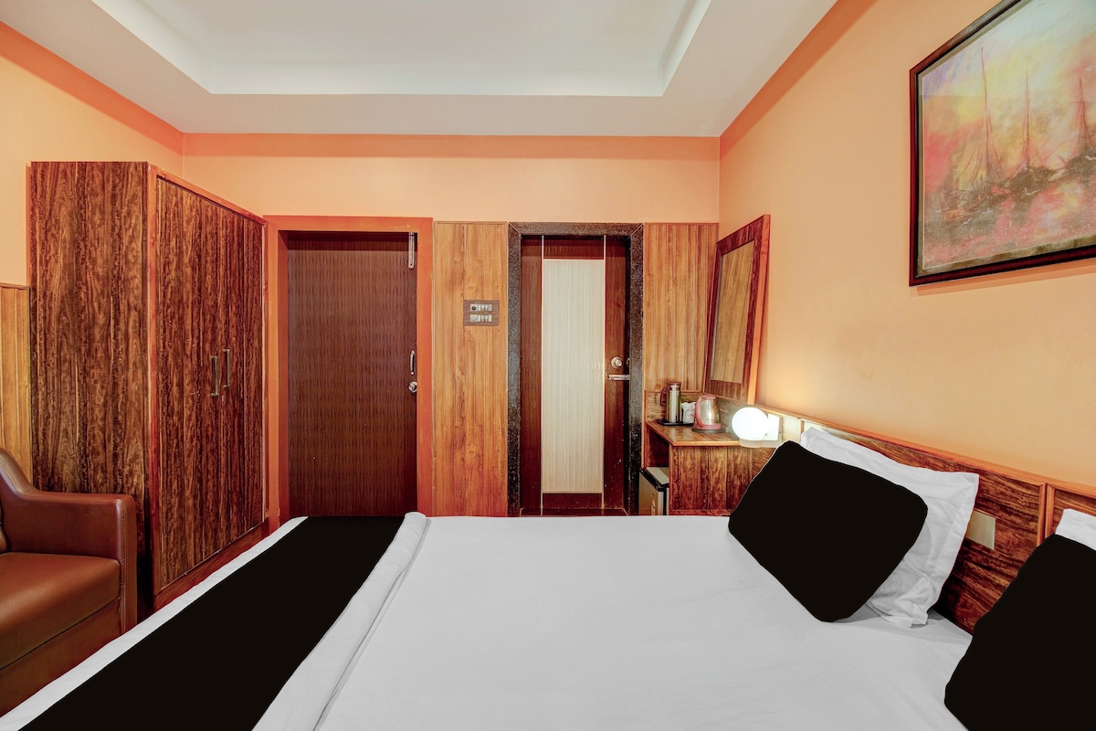A hotel room with a bed, a desk with a lamp, a chair, and a wardrobe.