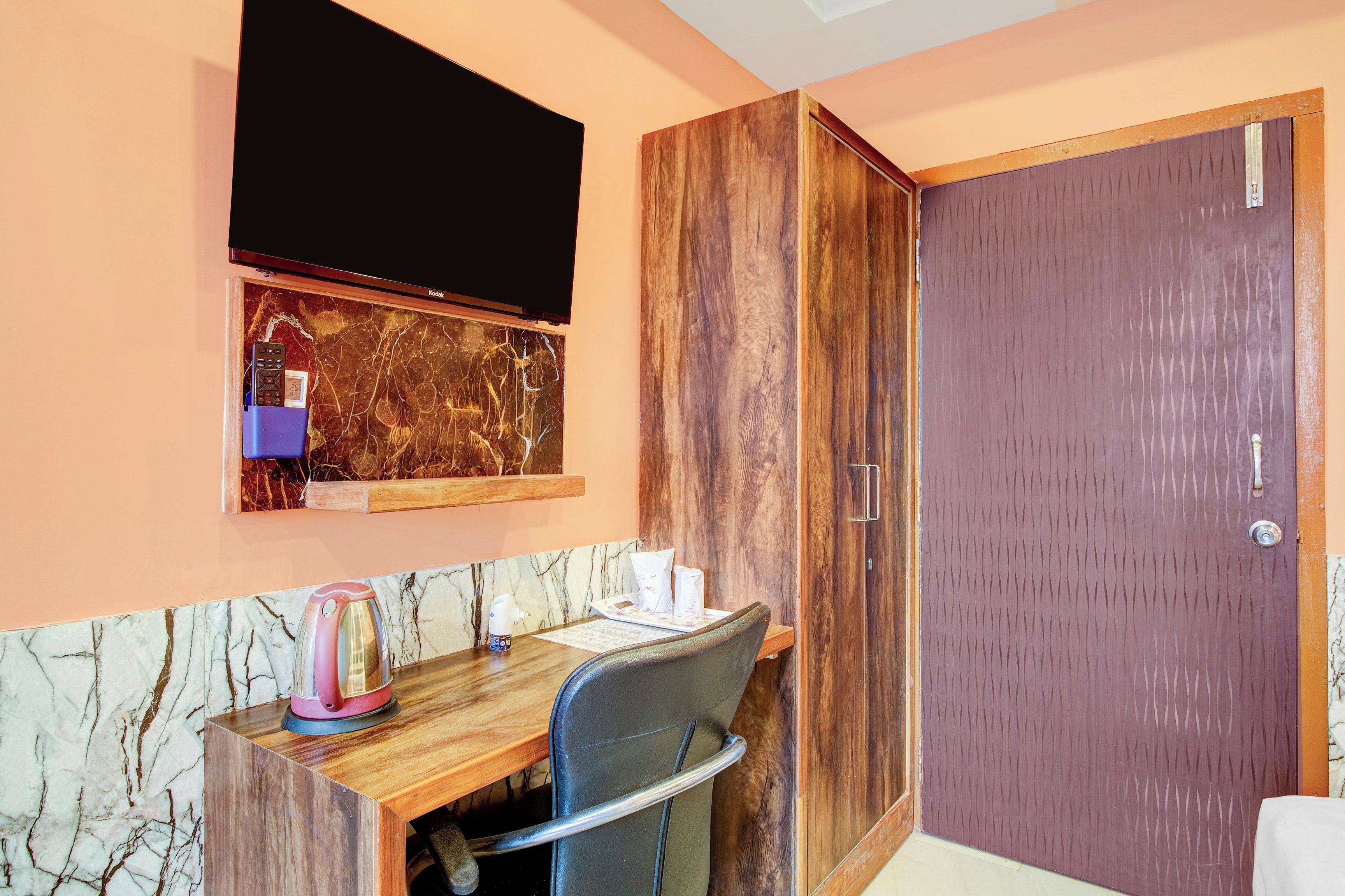 Een kamer met een houten bureau, een stoel, een aan de muur bevestigde televisie en een garderobe met spiegel.