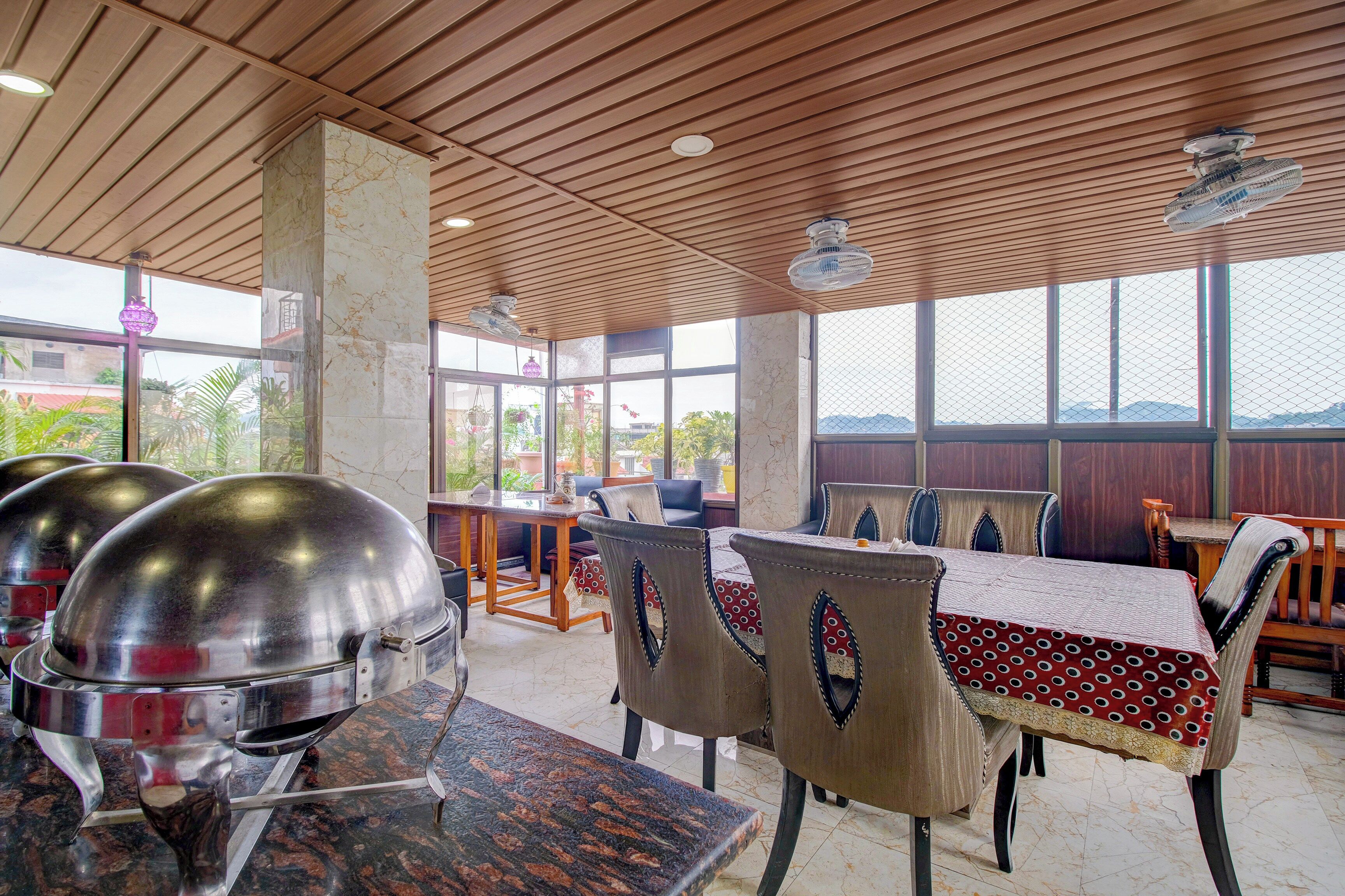 Un restaurante con pilares de mármol, techo de madera y amplios ventanales con vistas.