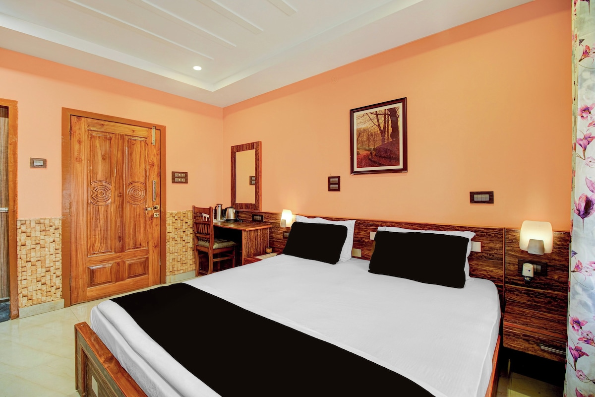 A hotel room with a large bed, a desk, a chair, a wooden wardrobe, a mirror, and a painting on the wall.