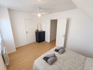 A bedroom with a bed, a dresser, a ceiling fan, and a door.