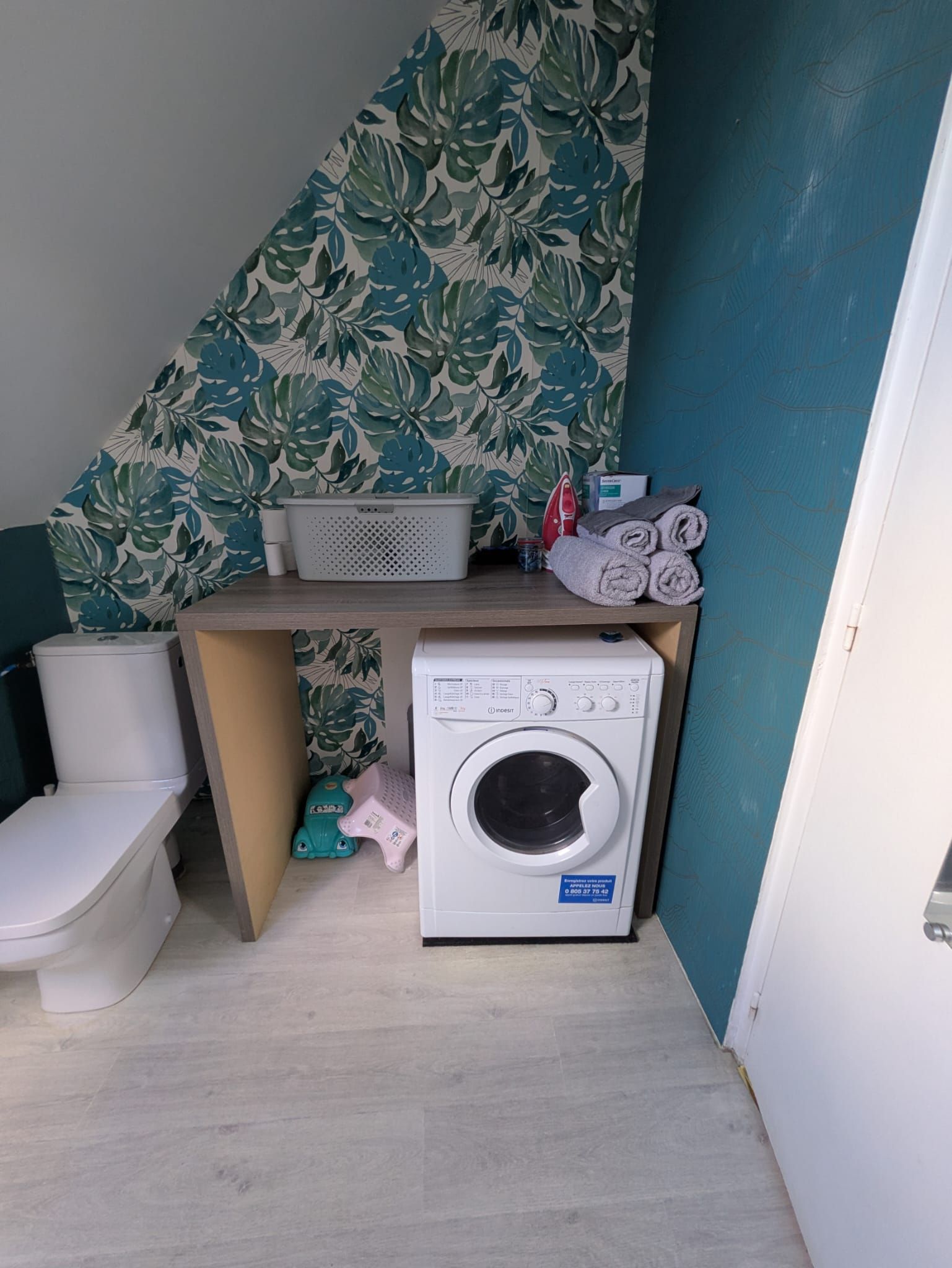 Una lavanderia funzionale con lavatrice, un WC e uno scaffale con asciugamani piegati.