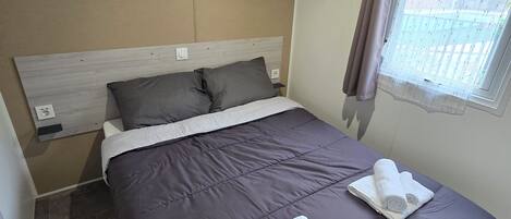 A neatly made bed with a grey duvet, two pillows, and two rolled towels on the bed.