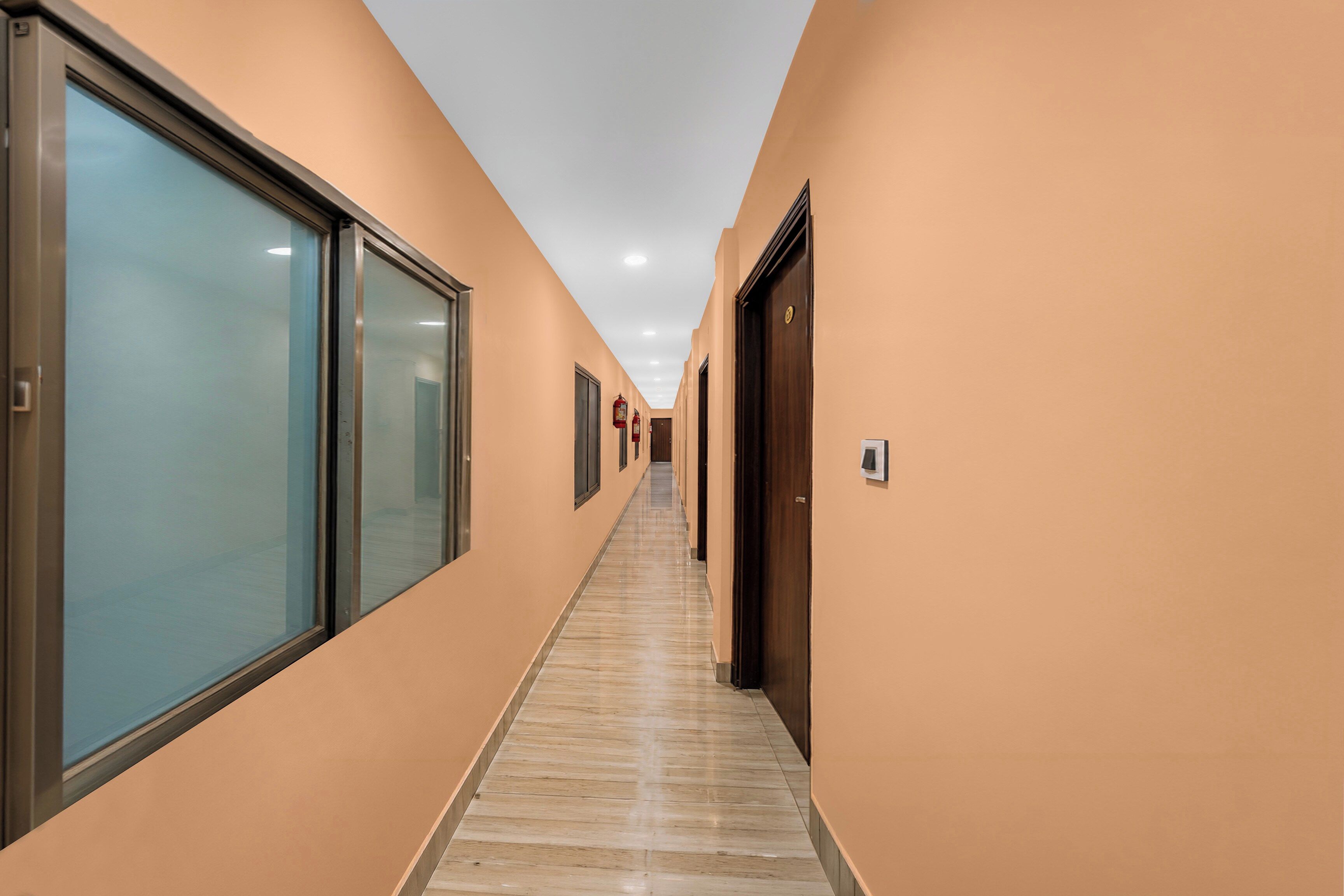 Un pasillo con puertas de vidrio a un lado y puertas de madera al otro, que conduce a un vestíbulo con piso de baldosas.