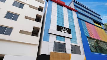 Un edificio de varios pisos con fachadas de blanco, azul y rojo, con amplias ventanas y un letrero destacado que dice 'Collection OYO-Serviced'.