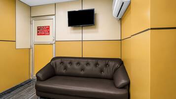 Un área de espera con un sofá de cuero marrón, una puerta cerrada, un televisor montado y una unidad de aire acondicionado en la pared.