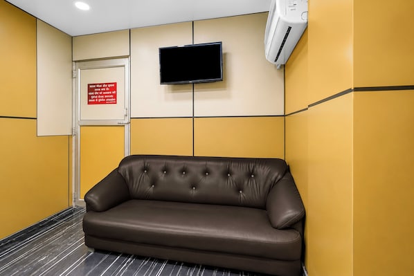Un área de espera con un sofá de cuero marrón, una puerta cerrada, un televisor montado y una unidad de aire acondicionado en la pared.