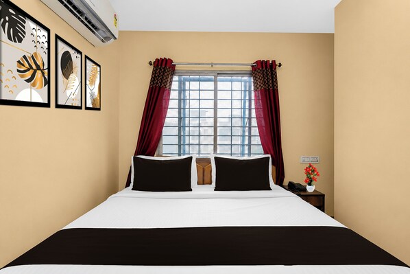 Una habitación de hotel con una cama, un ventanal con cortinas, un aire acondicionado instalado en la pared y cuadros enmarcados.