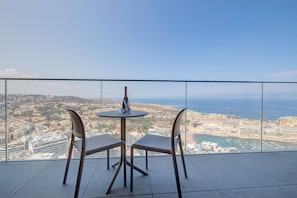 A balcony with a table and two chairs, overlooking a coastal cityscape with buildings and a marina. - Superlative Skyline Apartment, Mercury Tower (St. Julian's)