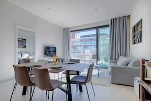 A modern living room with a dining area, a grey sofa, and a balcony with a view of buildings. - Mercury Tower Modern Apartment (St. Julian's)