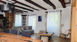 A living room with a sofa, a wooden table, and a chair. There is a bookshelf and a plant. - Country house at the foot of Turenne Castle (Turenne)