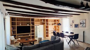 A living room with a large TV, wooden shelves, a dining table with chairs, and a sofa. - Country house at the foot of Turenne Castle (Turenne)