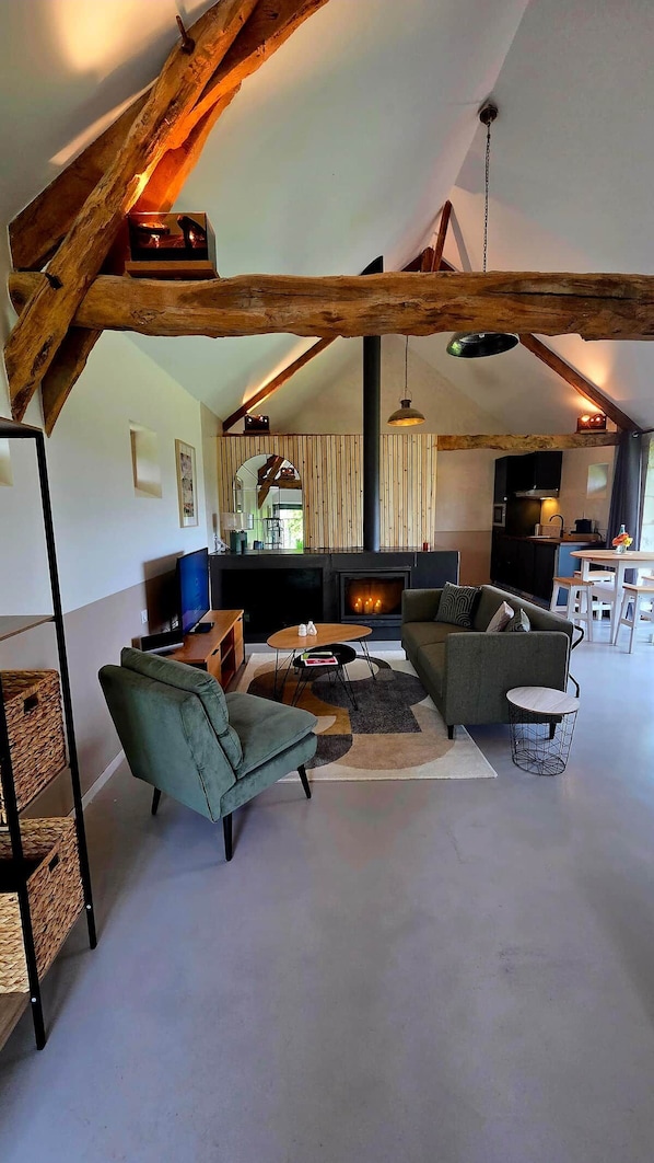 Un loft espacioso con vigas de madera a la vista, chimenea, televisor y zona de comedor.