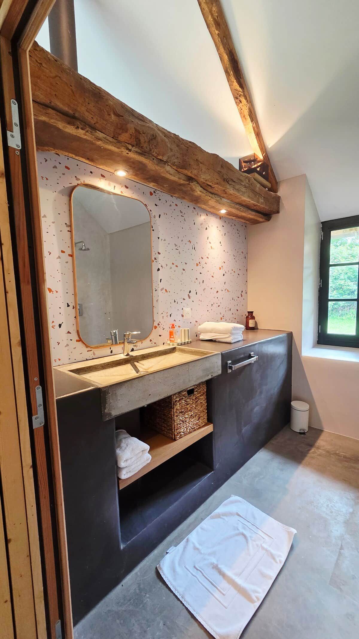A bathroom with a wooden ceiling, a large mirror, a sink with a towel rack, and a window.