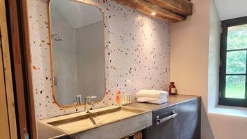 A bathroom with a wooden ceiling, a large mirror, a sink with a towel rack, and a window.
