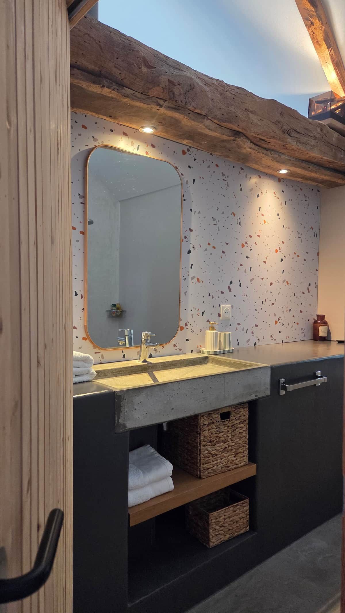 A bathroom with a wooden ceiling, a large mirror, a sink, and a towel rack.
