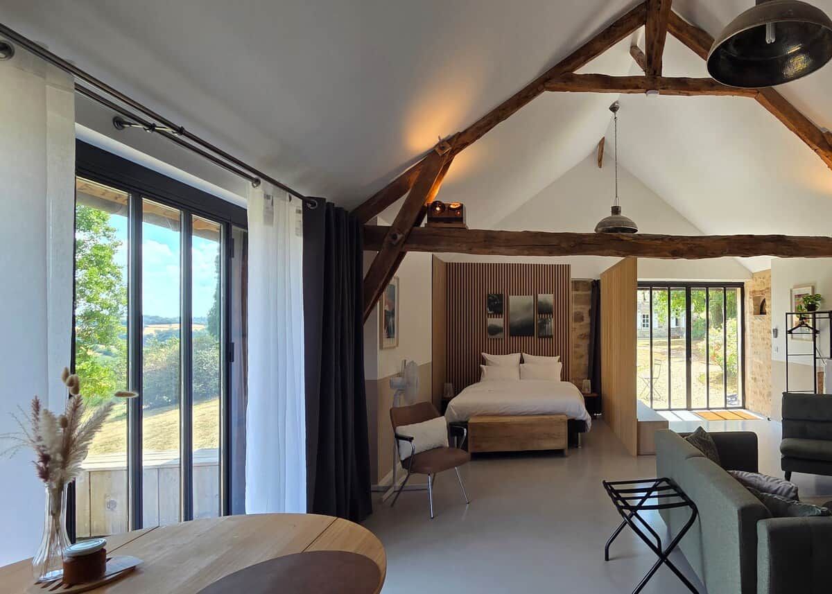 Een ruime slaapkamer met een groot bed, een zithoek met een bank en stoelen, en een eettafel met een bloevas.