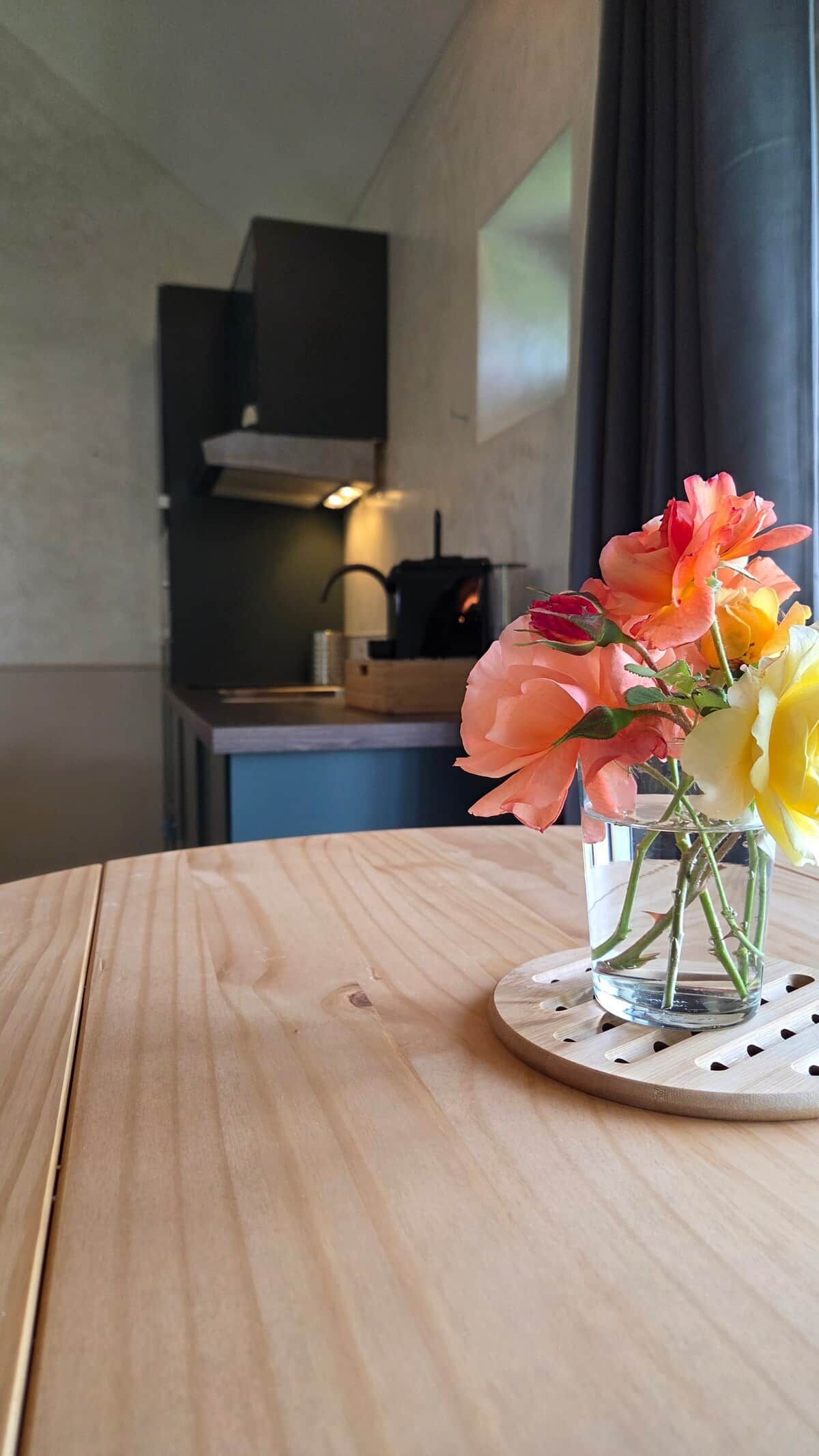 A wooden table with a clear glass vase containing flowers.