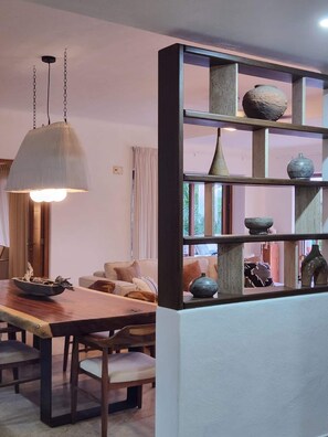 A dining area with a wooden table and chairs, a hanging light fixture, and a bookshelf with decorative items. - Esta amplia villa de 3 habitaciones ofrece espectaculares vistas al océano, una alberca privada tipo plunge, acceso directo a la playa y acceso a las increíbles amenidades del resort, incluyendo 8 albercas, spa,  restaurante y mucho mas (Cruz de Huanacaxtle)