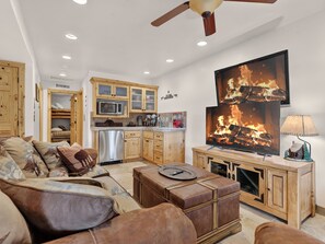 Ein Wohnzimmer mit einer Couch, Hocker, Holzschränken, einem Fernseher und einem Kamin.