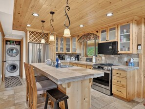 A modern kitchen with wooden cabinets, a central island, stainless steel appliances, and pendant lighting. - Chair 5 Chalet | True Ski In/ Ski Out + Hot Tub (Brian Head)