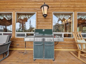 A wooden cabin with a Weber Genesis grill, wicker chairs, and a view of trees through the windows. - Chair 5 Chalet | True Ski In/ Ski Out + Hot Tub (Brian Head)