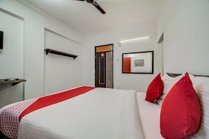 A hotel room with a bed, a desk, a ceiling fan, a door, and a framed picture on the wall. - Hotel O JNTU college Near LULU mall (Hyderabad)