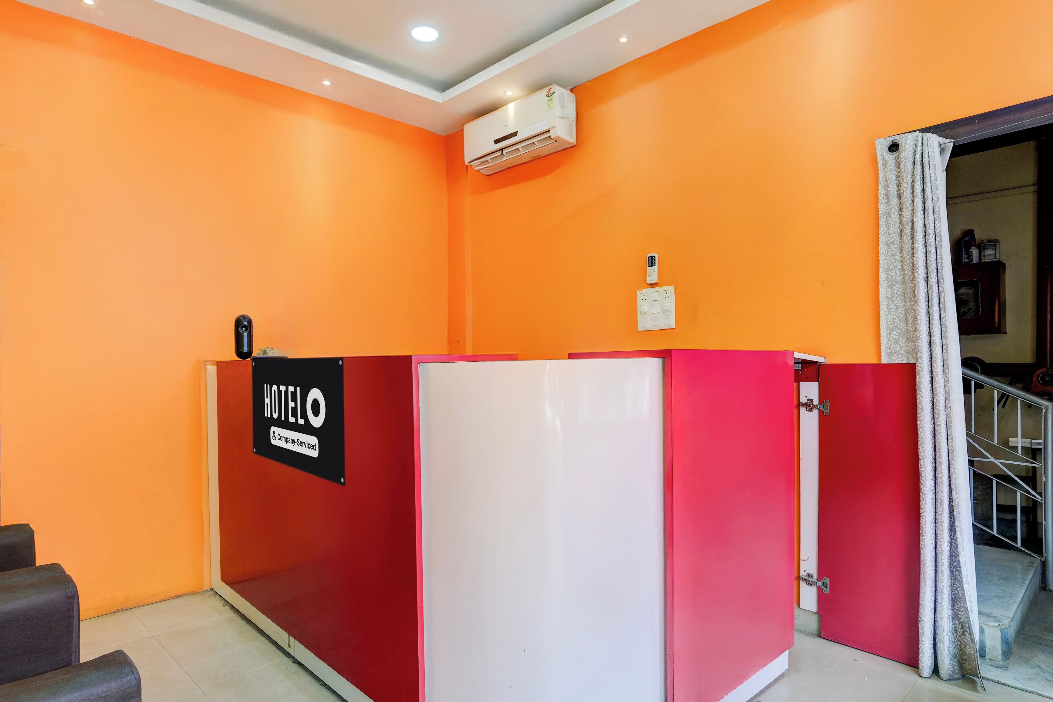 A hotel reception area with a red and white desk, an air conditioning unit, and a sign indicating company service.