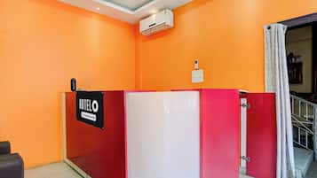 A hotel reception area with a red and white desk, an air conditioning unit, and a sign indicating company service.