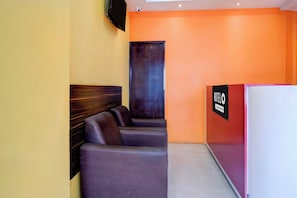 A hotel lobby with a reception desk, a seating area with cushioned chairs, and a wall-mounted television. - Hotel O Sankaradeva Kalakshetra (Guwahati)