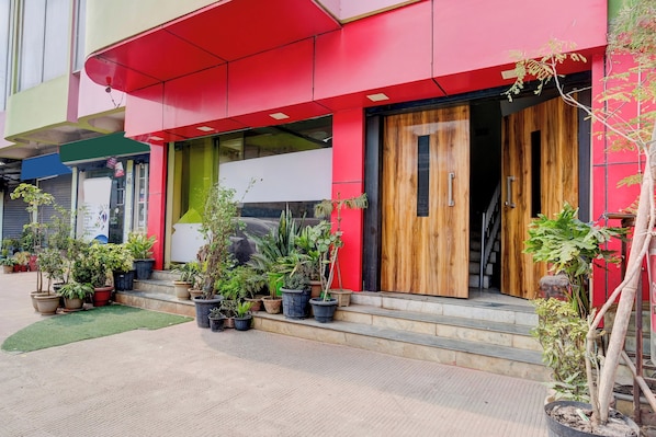 Un edificio con fachada roja, puerta de madera y varios maceteros a nivel de calle.
