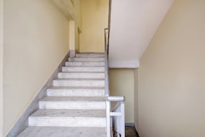 A staircase with marble steps leading upwards, a handrail on the right, and a plain wall on the left. - Hotel O Sankaradeva Kalakshetra (Guwahati)