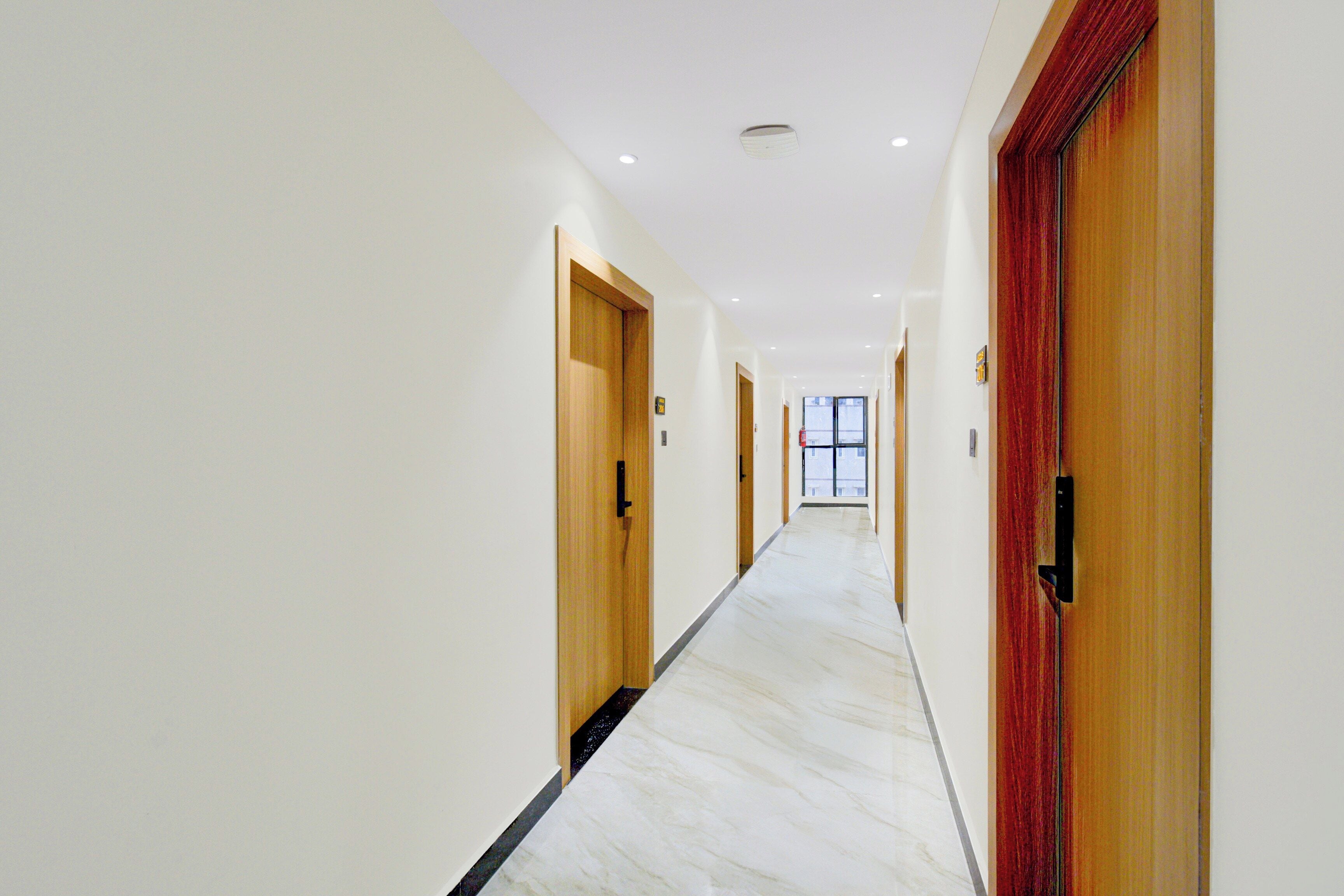 A hotel corridor with doors on both sides, a marble floor, and a ceiling with recessed lighting.