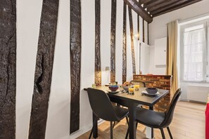 A dining area with a wooden table, black chairs, and a brick accent wall. - Charming Parisian Studio in the Heart of Paris 5th (Paris)