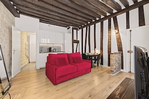 A modern living room with a red sofa, wooden flooring, and exposed wooden beams. - Charming Parisian Studio in the Heart of Paris 5th (Paris)